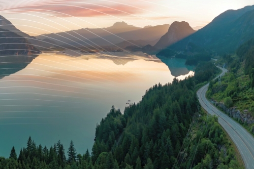 A BC lake at sunset with a highway running beside it and mountains in the distance
